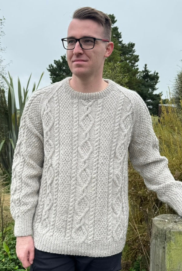 Man leaning on fence wearing Lesley Unisex Aran Wool sweater in the colour Oatmeal.