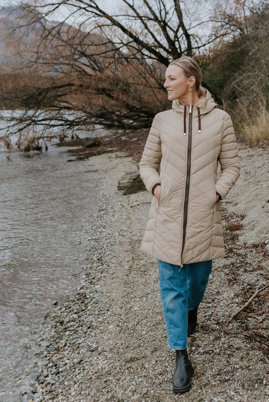 Woman wearing Moke - Arnie Reversible Packable Down Coat (ARNIE) in colour Chocolate/Palomino walking on lakefront.