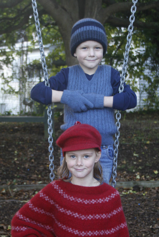 Boy wearing light blue colour vest, standing behind girl on a swing.