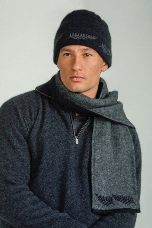Man standing wearing a black coloured Koru Silver Fern Accessory Set of scarf, gloves, and beanie.