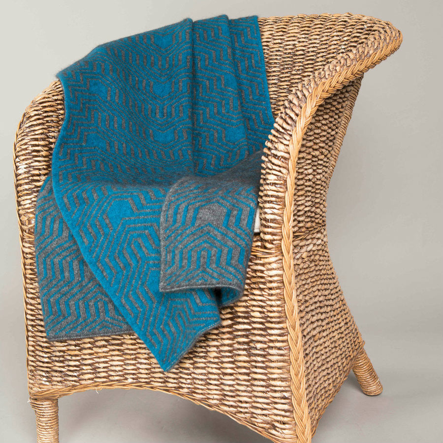 Grey and pacific-coloured Koru Merino and Possum Patterned Throw draped over chair.