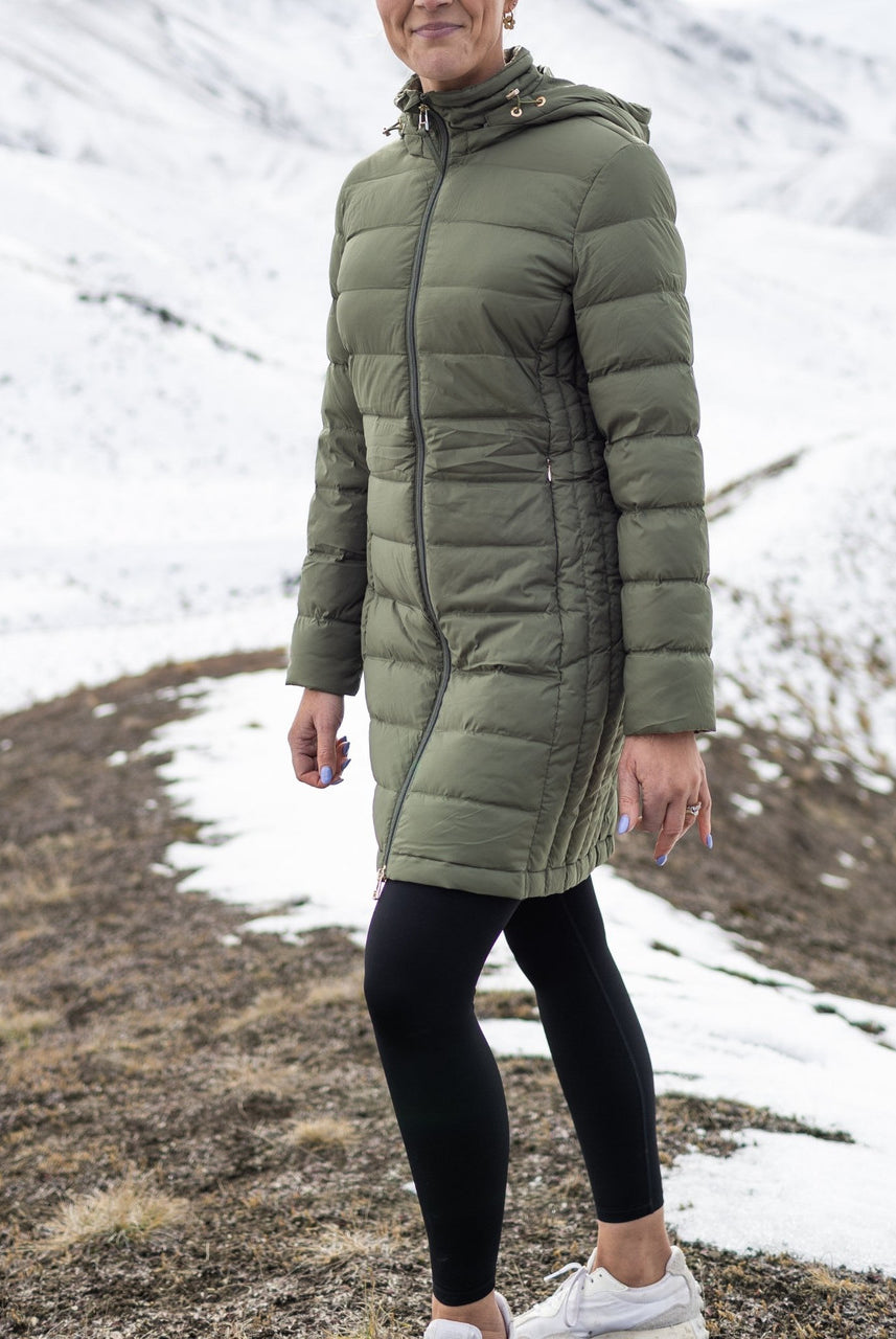 Woman wearing Moke - Sydney Cloud Touch 90/10 Down Coat (SYDNEY) in the colour Olive Green on a hill with snow in the background.
