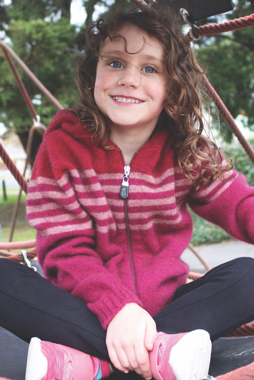 Girl sitting wearing fuchsia colour striped hoodie.