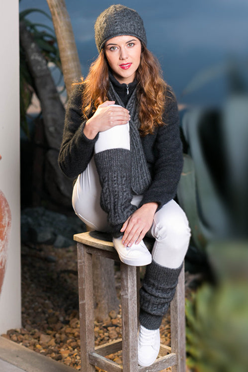 Woman sitting outside wearing grey Koru cable leg warmers.