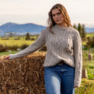Woman leaning on hay wearing Lesley Unisex Aran Wool sweater in the colour Oatmeal.