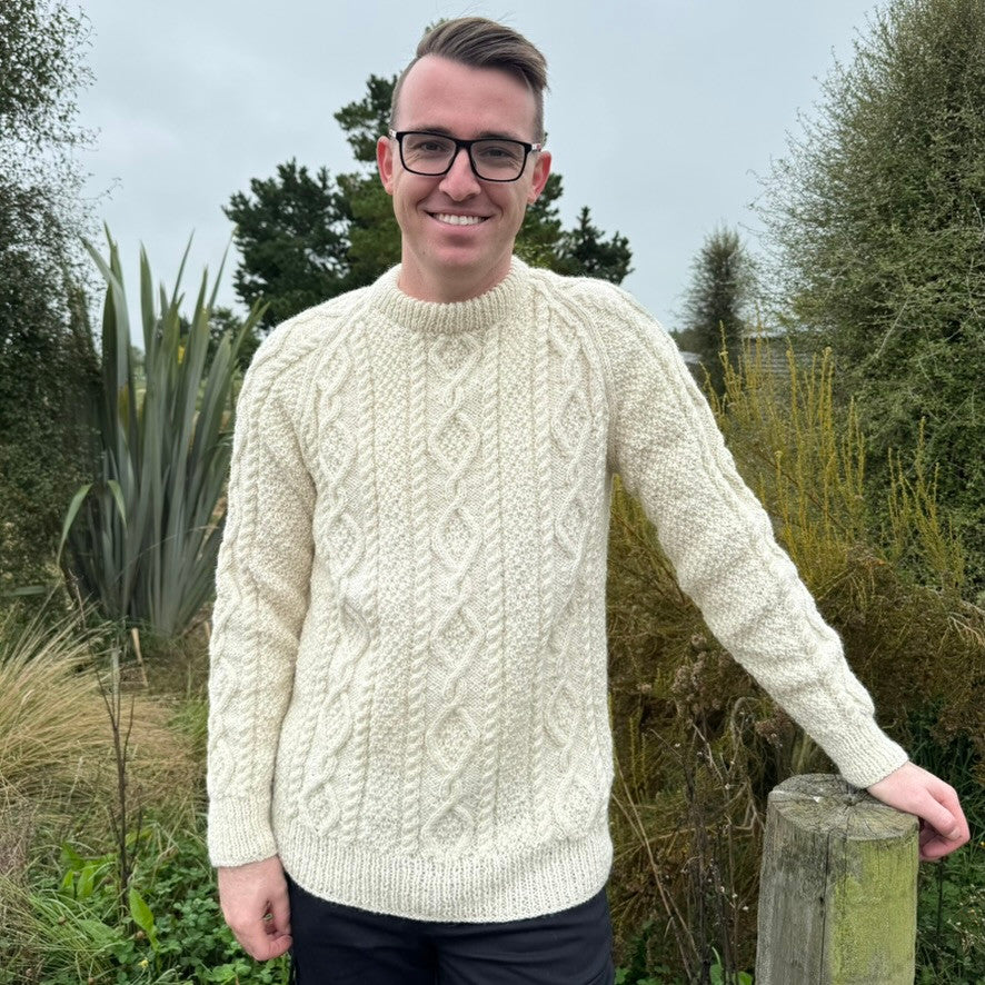 Man leaning on fence wearing Lesley Unisex Aran Wool sweater in the colour Cream.