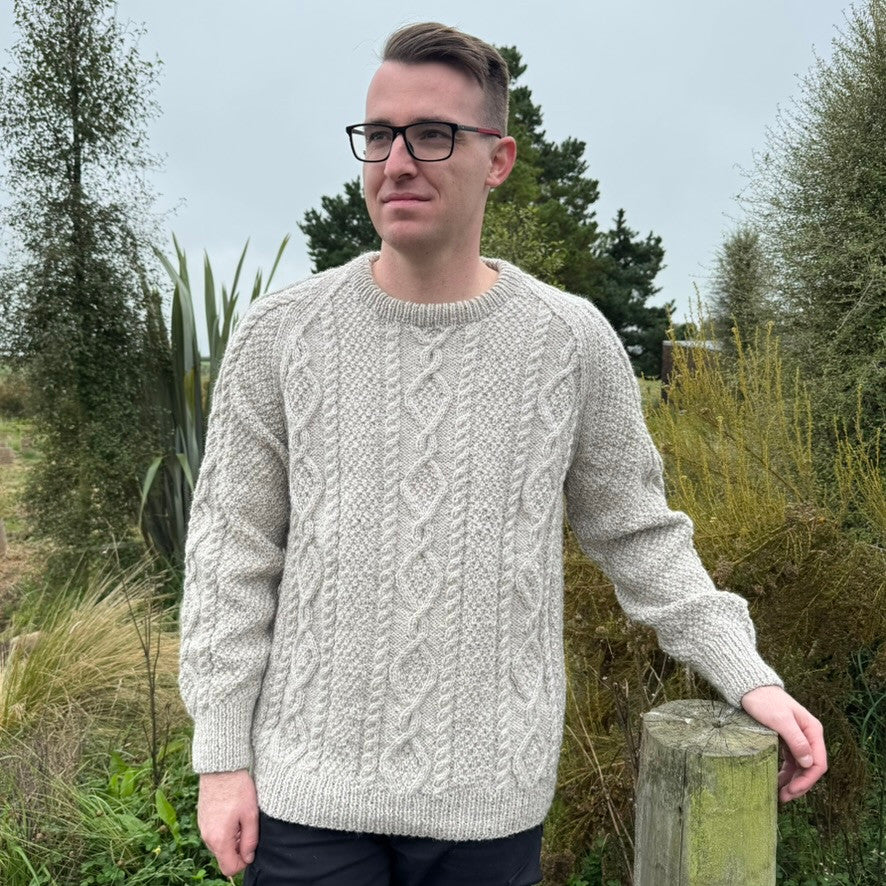 Man leaning on fence wearing Lesley Unisex Aran Wool sweater in the colour Oatmeal.