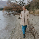 Woman wearing Moke - Arnie Reversible Packable Down Coat (ARNIE) in colour Chocolate/Palomino walking on lakefront.