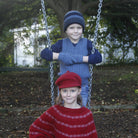Boy wearing light blue colour vest, standing behind girl on a swing.