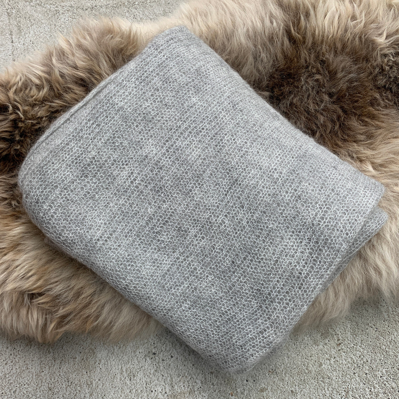 Folded silver-coloured Knight Mohair Throw on fur rug.