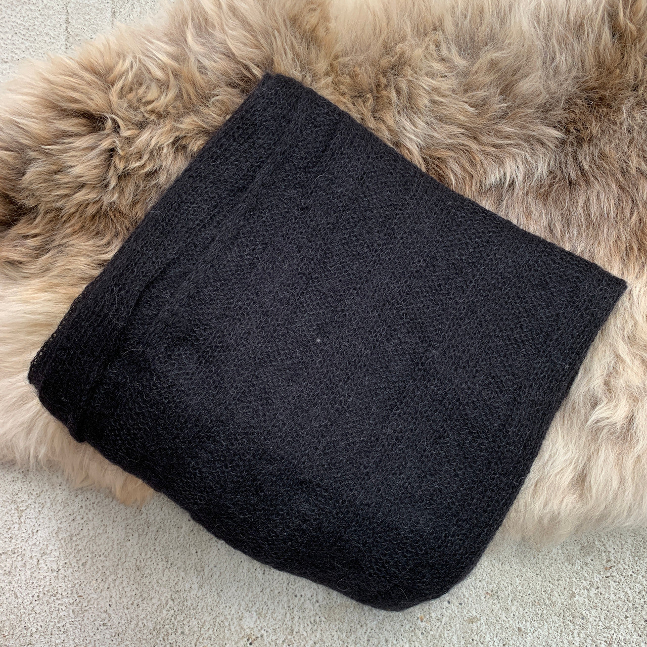 Folded black-coloured Knight Mohair Throw on fur rug.