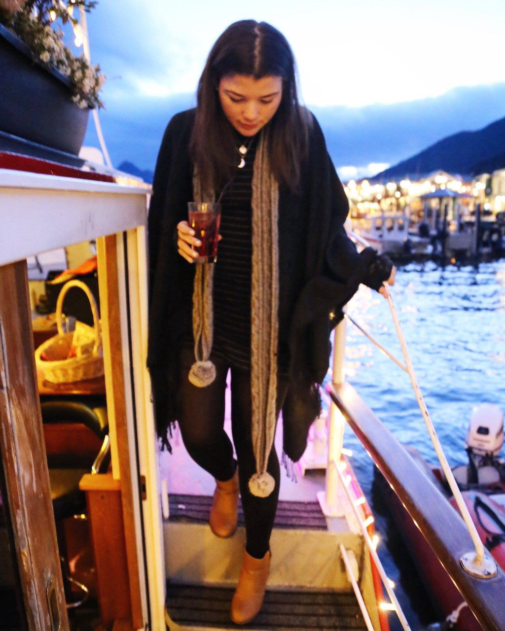 Woman walking on boardwalk wearing scarf with pom poms.