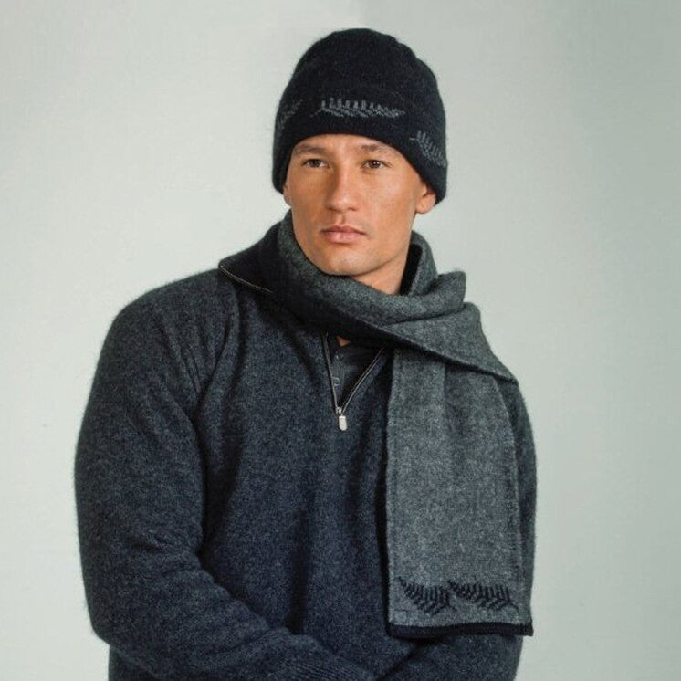 Man standing wearing a black coloured Koru Silver Fern Accessory Set of scarf, gloves, and beanie.