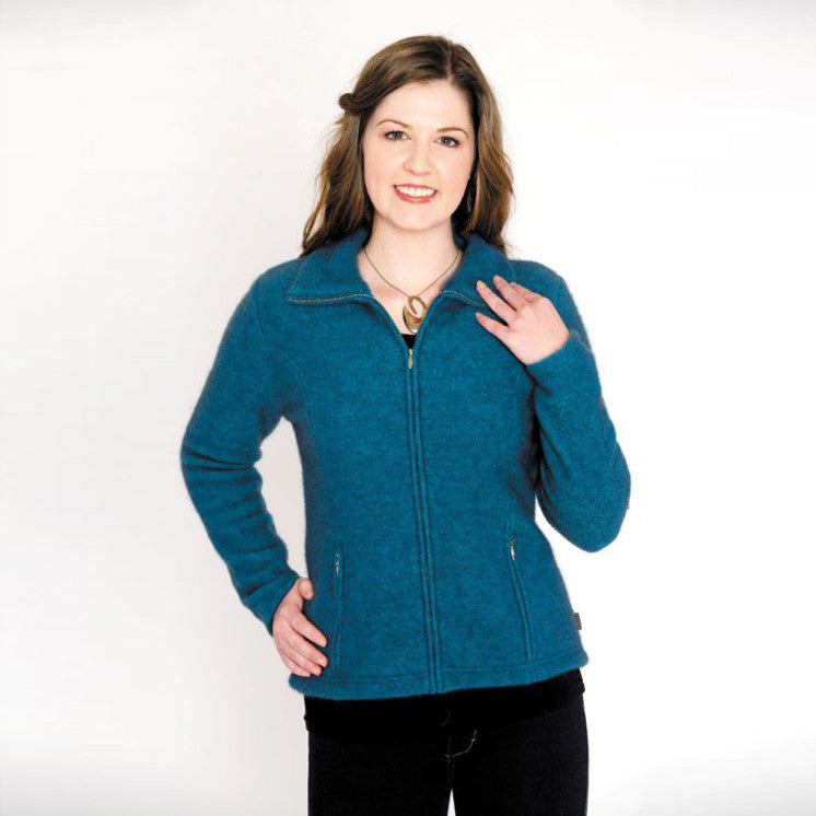 A woman standing wearing a pacific-coloured Koru merino and possum Shaped Zip Jacket.