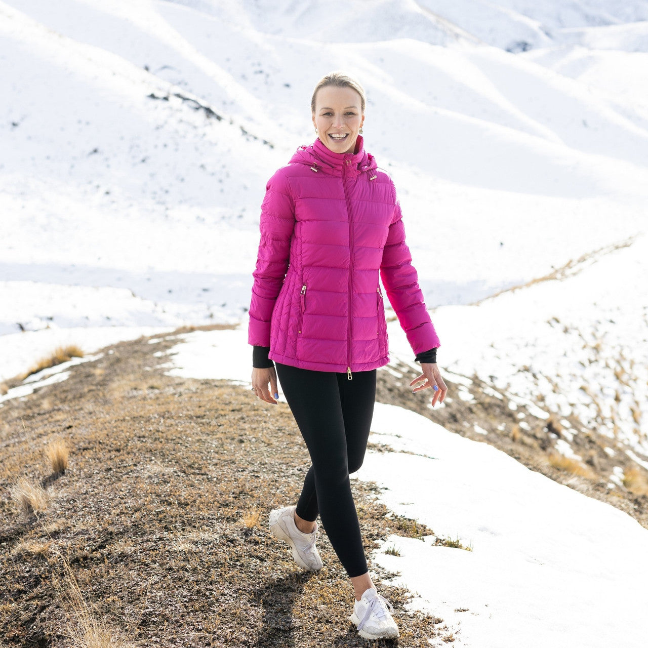 Woman wearing Moke - Lucy Cloud Touch Packable Down Jacket (LUCY) in the colour Rose Violet on a hill with snow in the background.