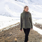 Woman wearing Moke - Lucy Cloud Touch Packable Down Jacket (LUCY) in the colour Olive Green on a hill with snow in the background.