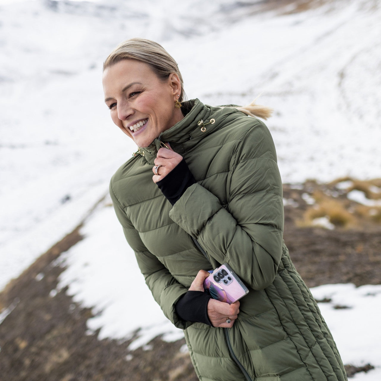 Woman wearing Moke - Sydney Cloud Touch 90/10 Down Coat (SYDNEY) in the colour Olive Green on a hill with snow in the background.
