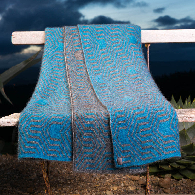 Grey and pacific-coloured Koru Merino and Possum Patterned Throw draped over bench.